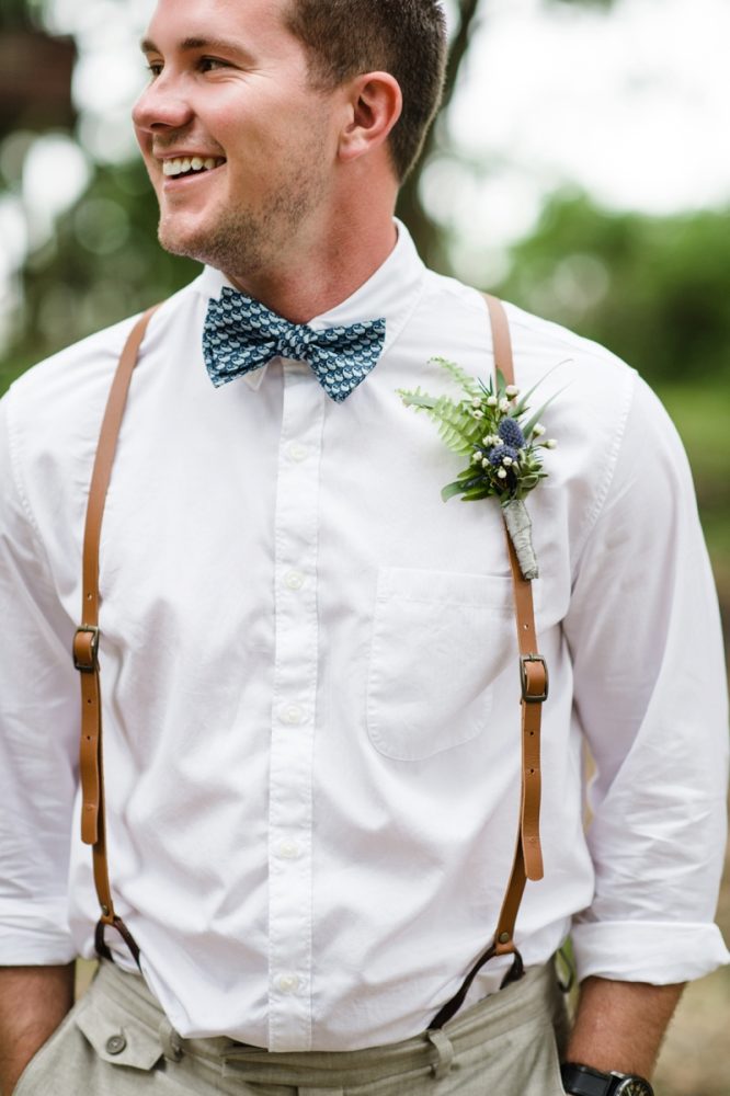 Groom wearing blue patterned bow tie and leather suspenders