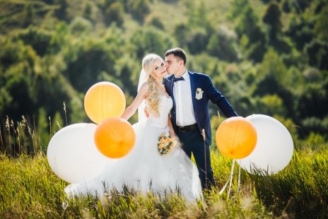 Bride and groom holding balloons in a field