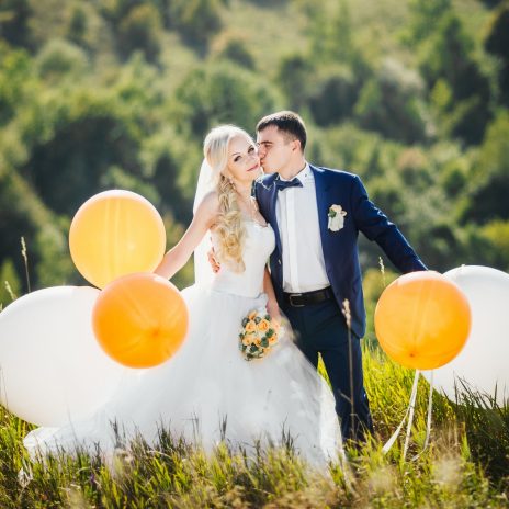 Bride and groom holding balloons in a field