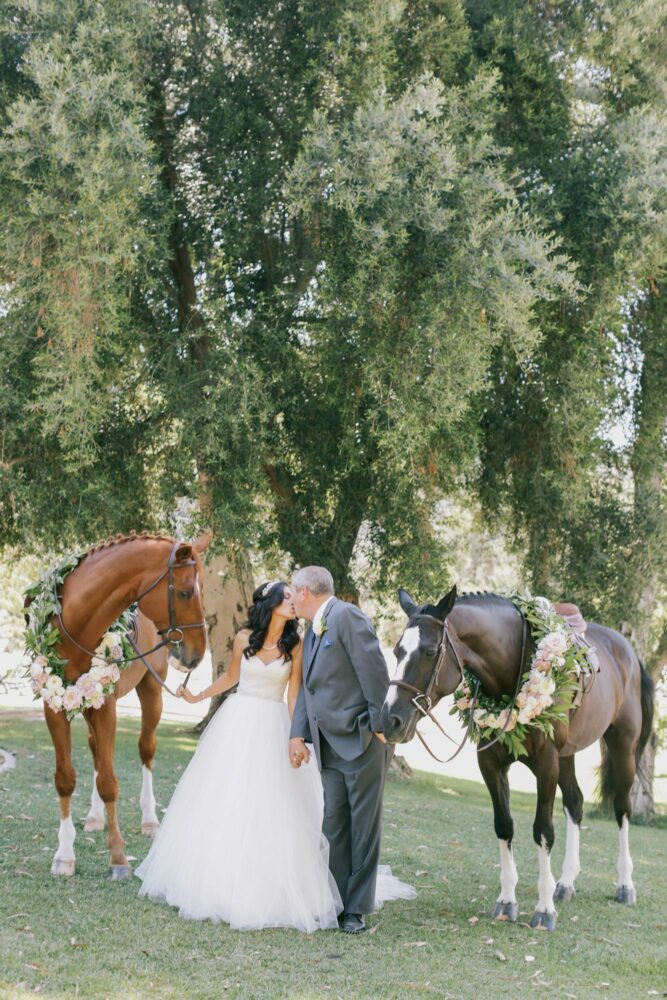 Bride and groom kissing between horses