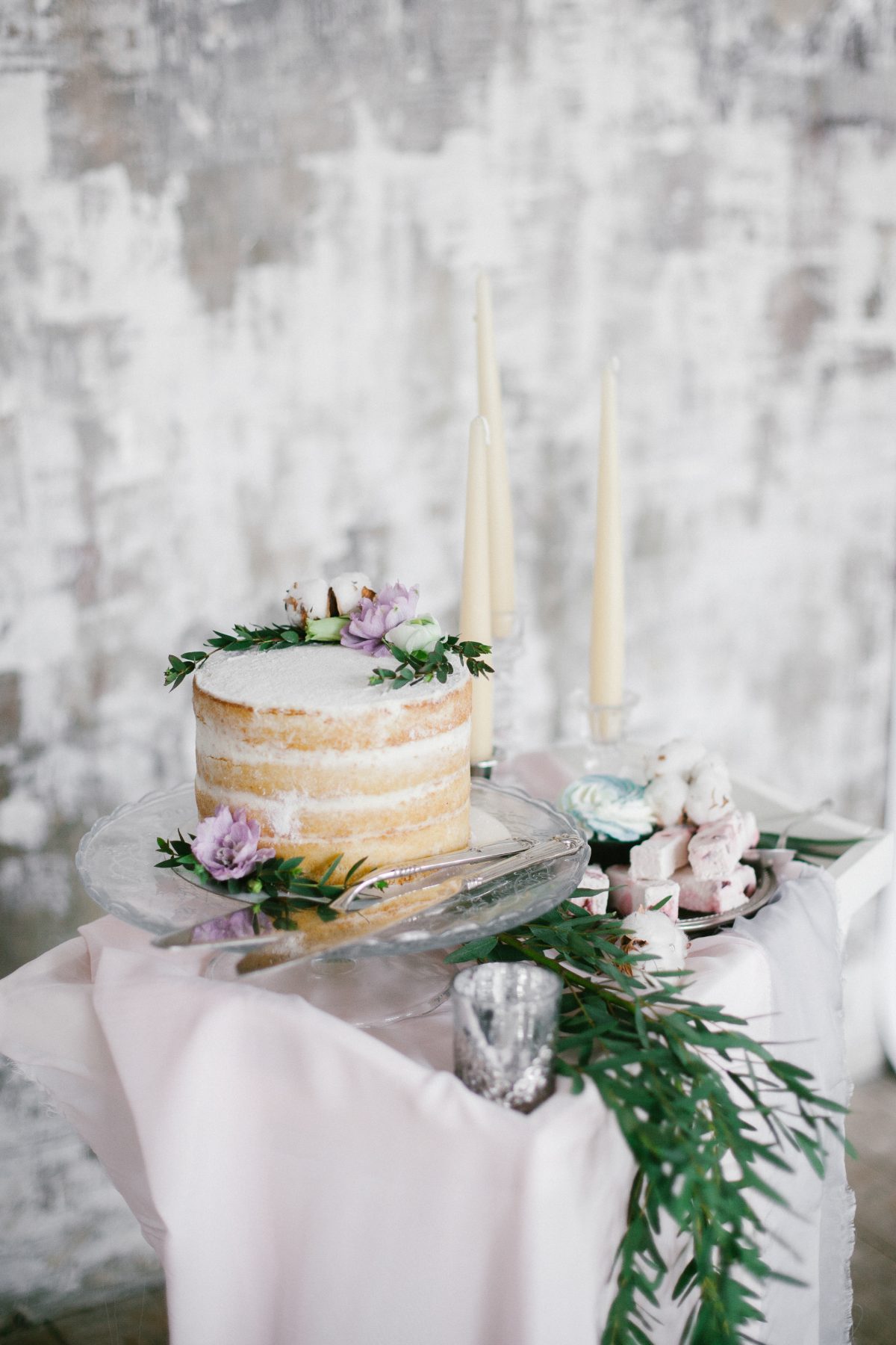 Beautiful naked wedding cake on table with grey washed wall behind it