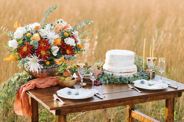A golden autumn tablescape design with rustic elements and fall fruits in a beautiful field at sunset by Aperture Vision Photography